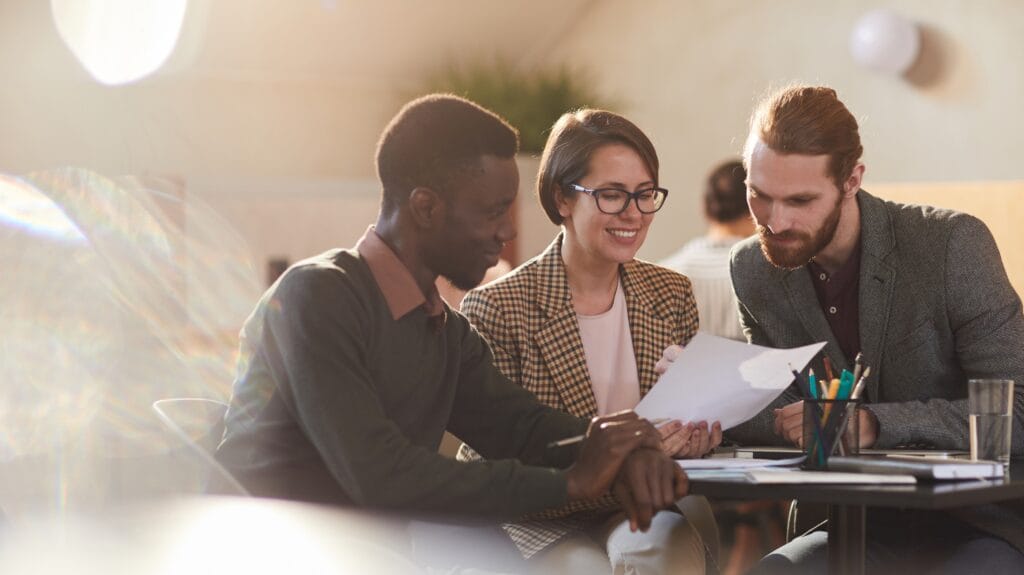 A group of 3 people in a meeting discussing notes.